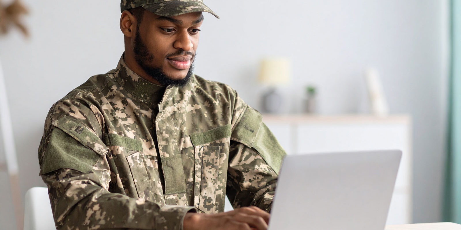 man-on-military-uniform-searching-the-web-on-a-laptop,-seating-on-a-table-at-home man-on-military-uniform-searching-the-web-on-a-laptop,-seating-on-a-table-at-home